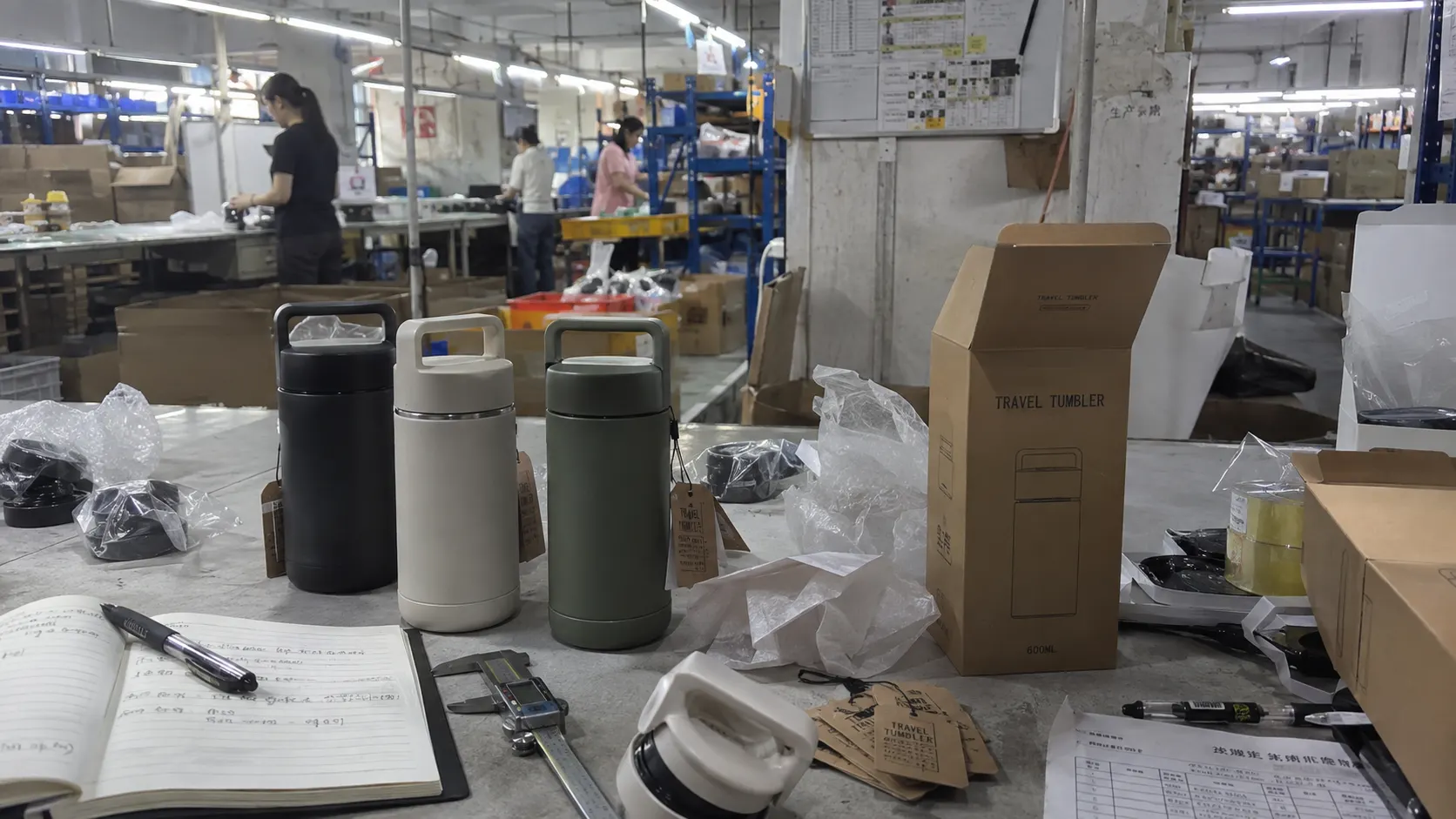 Samples, hang tags and printed retail boxes on a bench inside a factory in China, with the production line working behind